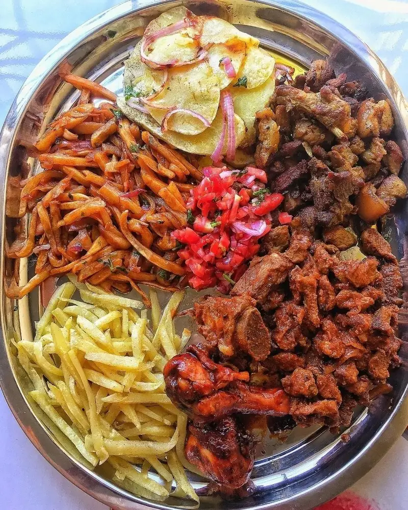 The Nyama Platter from above: mbuzi, pork, chicken drumsticks, plain fries, masala fries, Lyonnaise potatoes and kachumbari on a steel tray